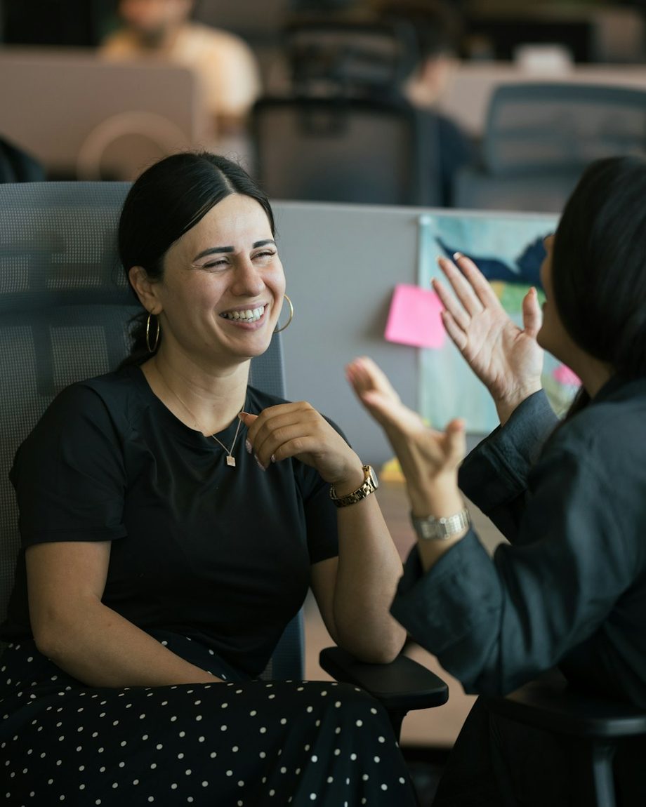 A manager laughing with someone on her team, mid-conversation at their desks.